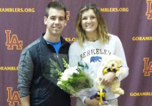 A man and woman celebrating college signing day with flowers and a teddy bear.