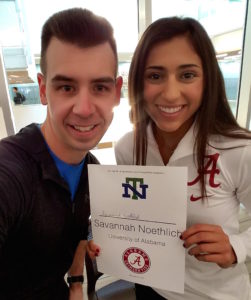 A man and a woman smiling while holding a sign on college signing day.