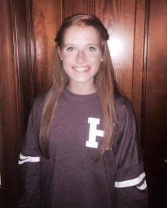 A young woman in a maroon sweater smiles for the camera on college signing day.