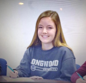 A girl participating in college signing day, sitting at a table with a pen and paper.