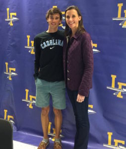 A man and woman posing for a picture in front of a college signing day banner.