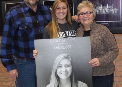 A group of people standing next to a picture of a lacrosse player during college signing day.