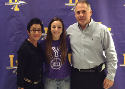 A couple posing for a picture in front of a purple banner at their college signing day.