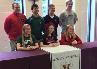 A group of people posing for a picture at a table during college signing day.