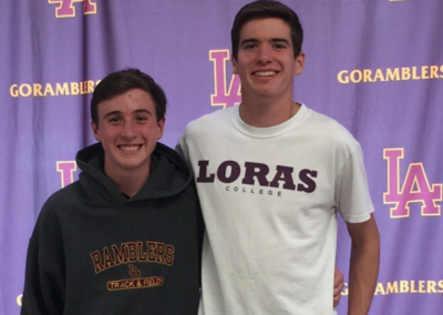 Two young men posing for a picture on college signing day in front of a purple banner.