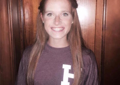 A girl in a maroon shirt smiles on college signing day.