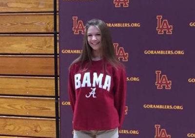 A girl in a maroon shirt celebrating college signing day in front of an Alabama banner.