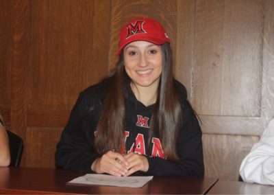 A girl wearing a hat celebrating college signing day at a table.