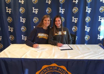 Two women sitting at a table on college signing day signing a letter of intent.