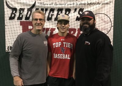 Three men posing for a picture in front of a baseball net on college signing day.