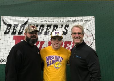 Three men posing for a picture after college signing day in a batting cage.