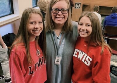 Three girls in red sweatshirts posing for a photo on college signing day in a classroom.