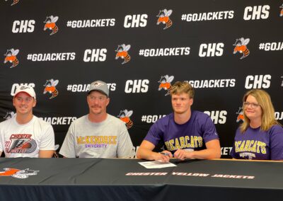 A group of people participating in college signing day, sitting at a table with a sign in front of them.