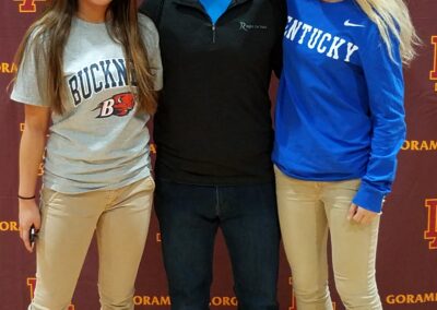 Three young people celebrating college signing day by posing for a picture in front of a banner.