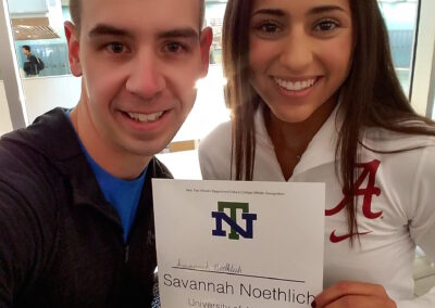 A man and a woman smiling while holding a college signing day sign.