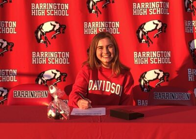 A young girl sitting at a table on college signing day, signing her letter of intent.