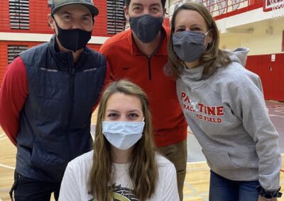 Four people wearing face masks posing for a picture during college signing day in a gym.