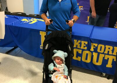 A man participates in college signing day with a baby in a stroller.