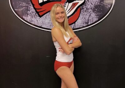 A woman in red shorts and white top standing next to a wall.