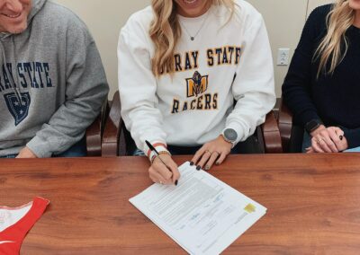 A woman signing papers at a table with two men.
