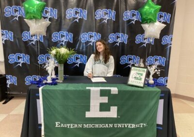 A woman sitting at the table signing her college letter of intent.