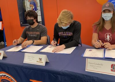 Three students sign their college letters at a table.